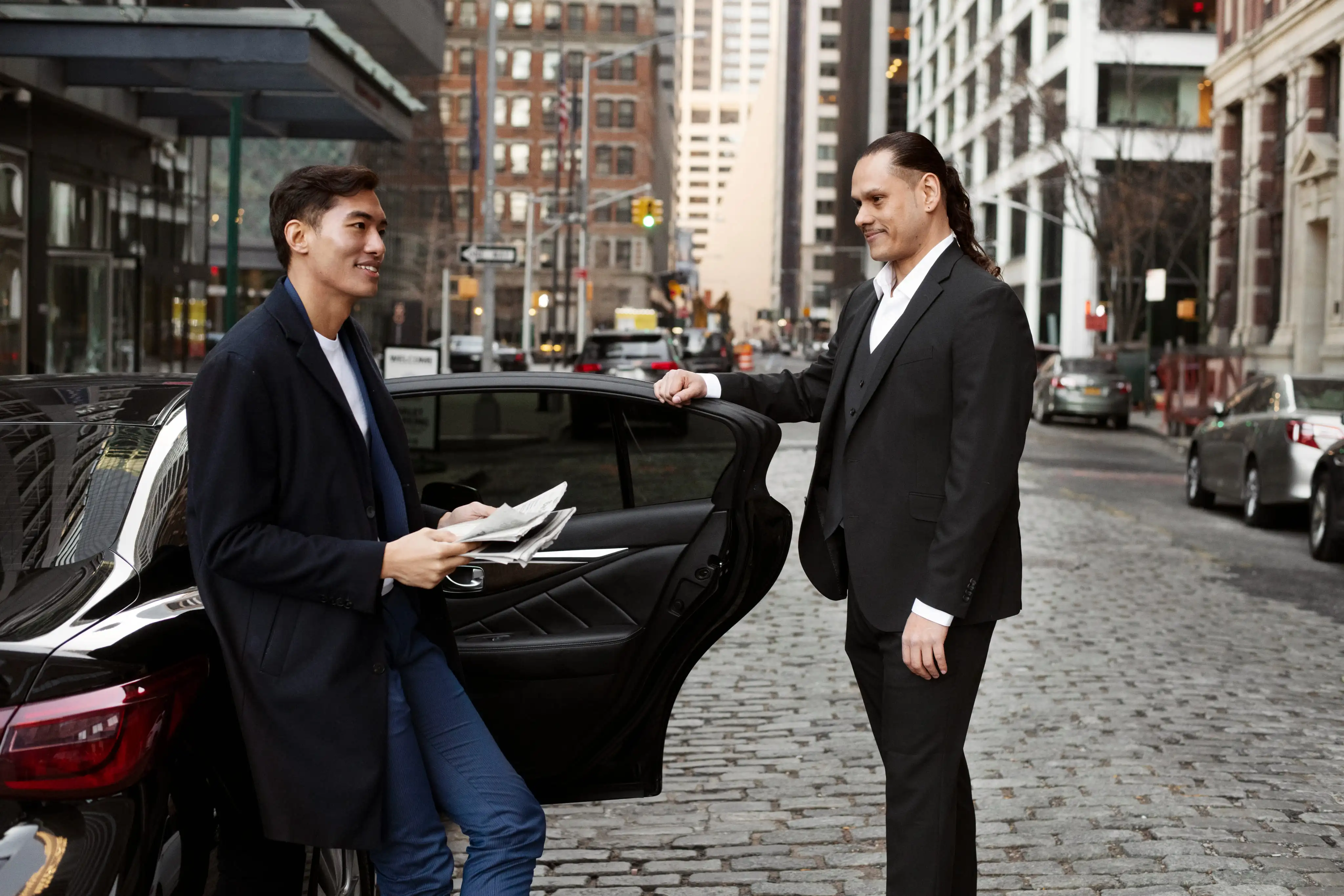 Chauffeur greeting a client beside a black car on arrival